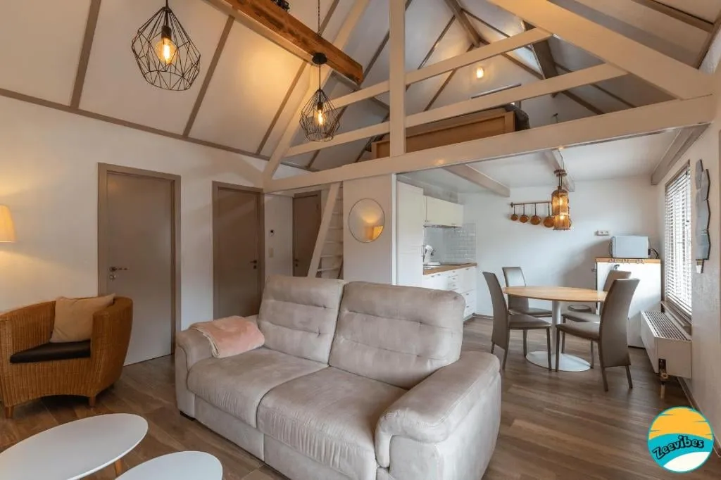 Wohnzimmer mit Sofa, Esstisch und sichtbaren Dachbalken