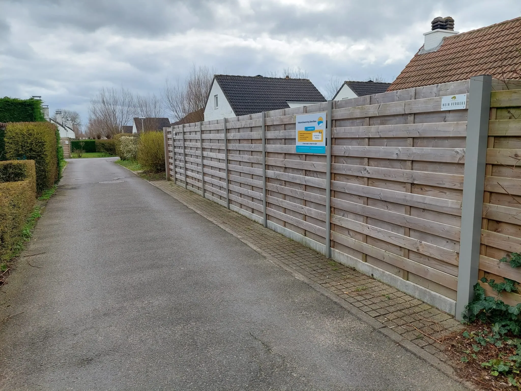 Das Sträßchen entlang des Hauses mit dem hohen Holzzaun