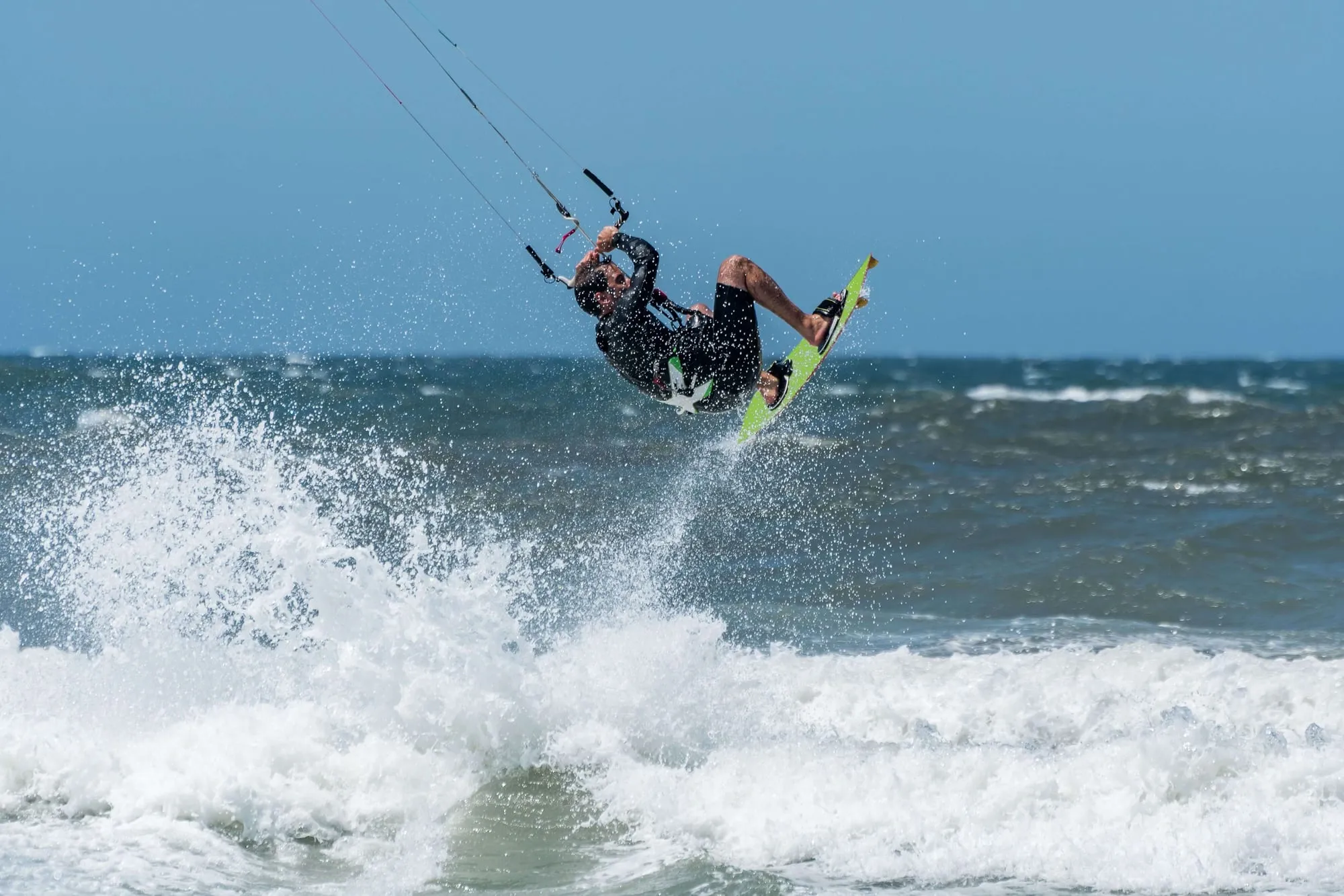 Een kitesurfer springt met een groen board hoog boven de golven