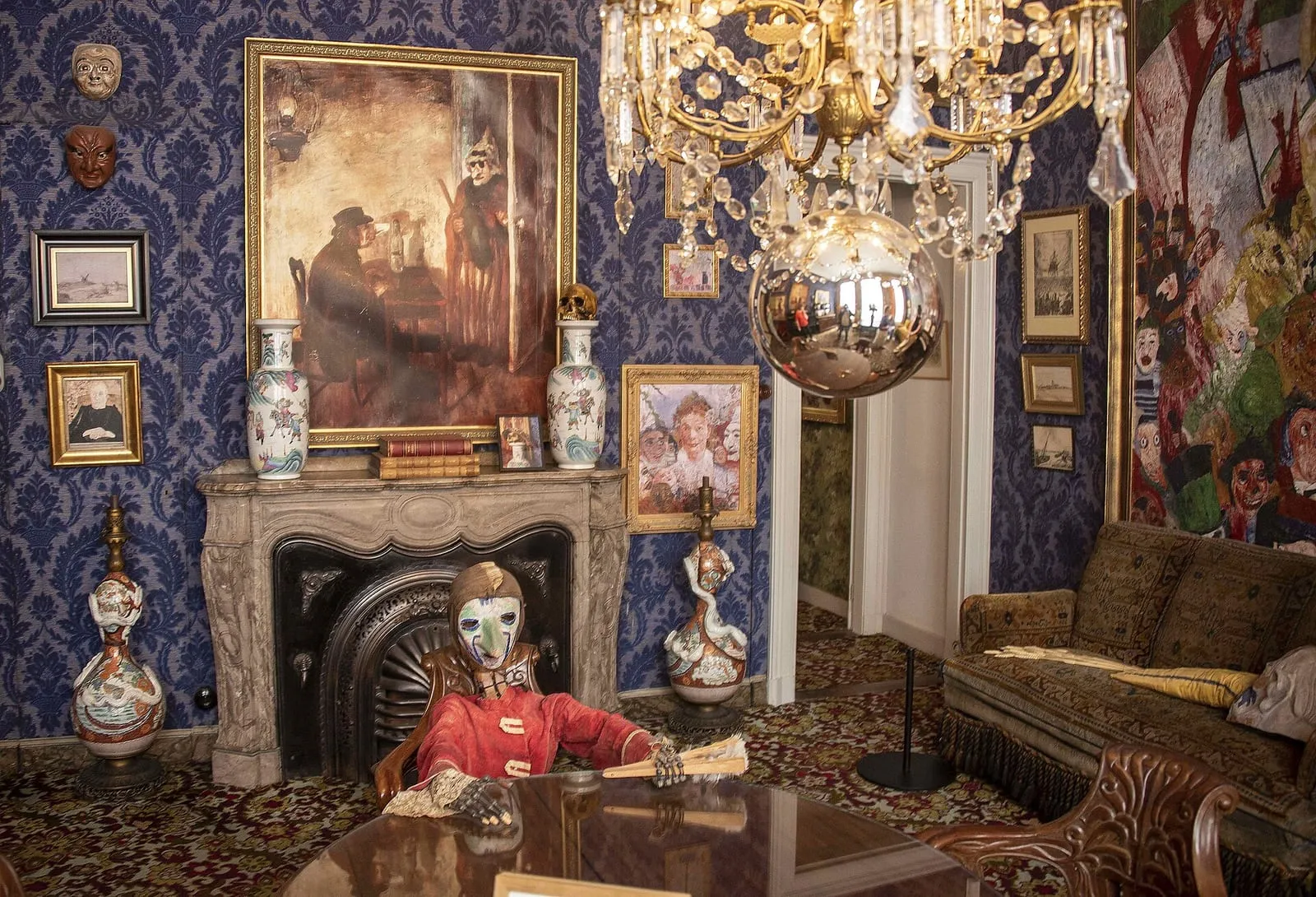 De blauwe salon van het Ensorhuis, met een schouw, schilderijen, een kroonluchter en vazen