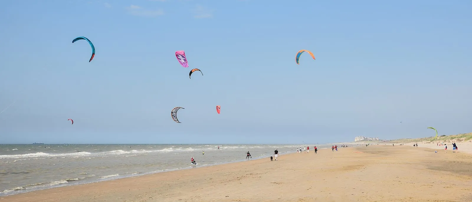 Kitesurfers met kleurrijke vliegers boven een breed strand en de zee