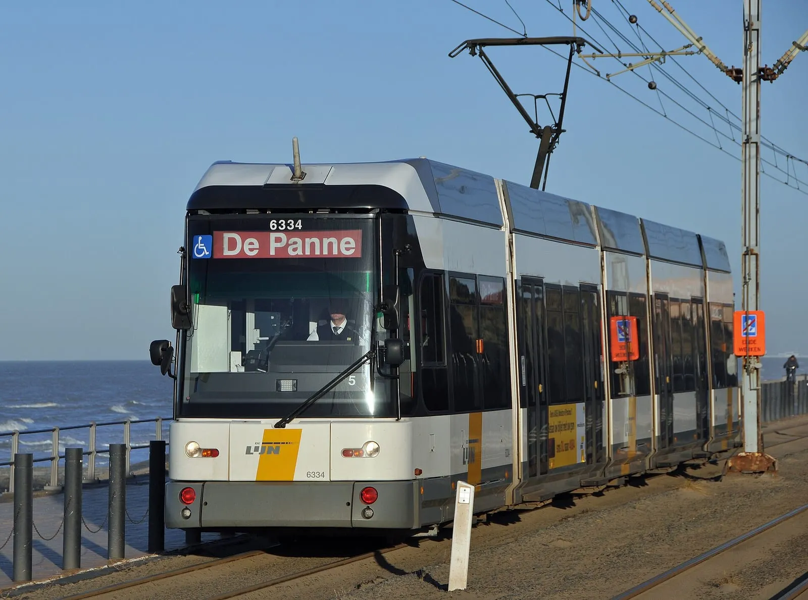 Een kusttram met bestemming De Panne rijdt langs de zeedijk, met de zee op de achtergrond