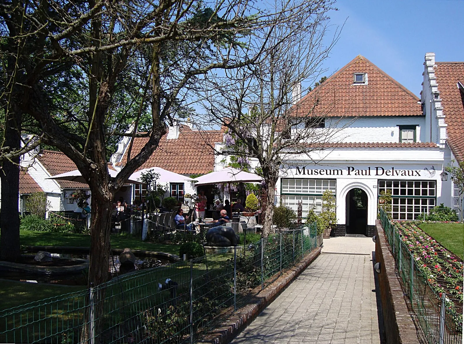 Het museum Paul Delvaux: een wit gebouw met rood pannendak aan een betegeld pad tussen het groen