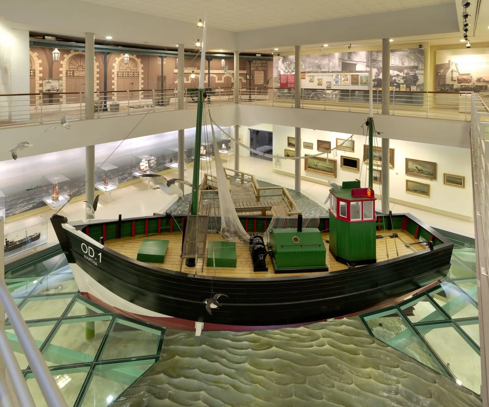Zaal van een visserijmuseum met een houten vissersschip op een glazen vloer