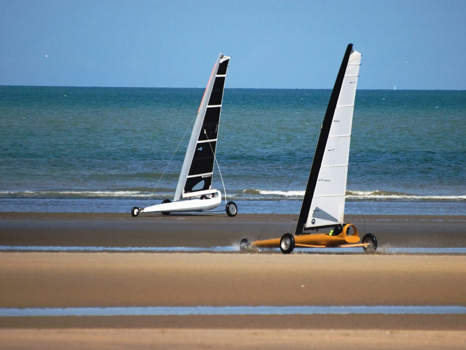 Twee strandzeilwagens met witte en zwarte zeilen rijden over het natte zand langs de zee