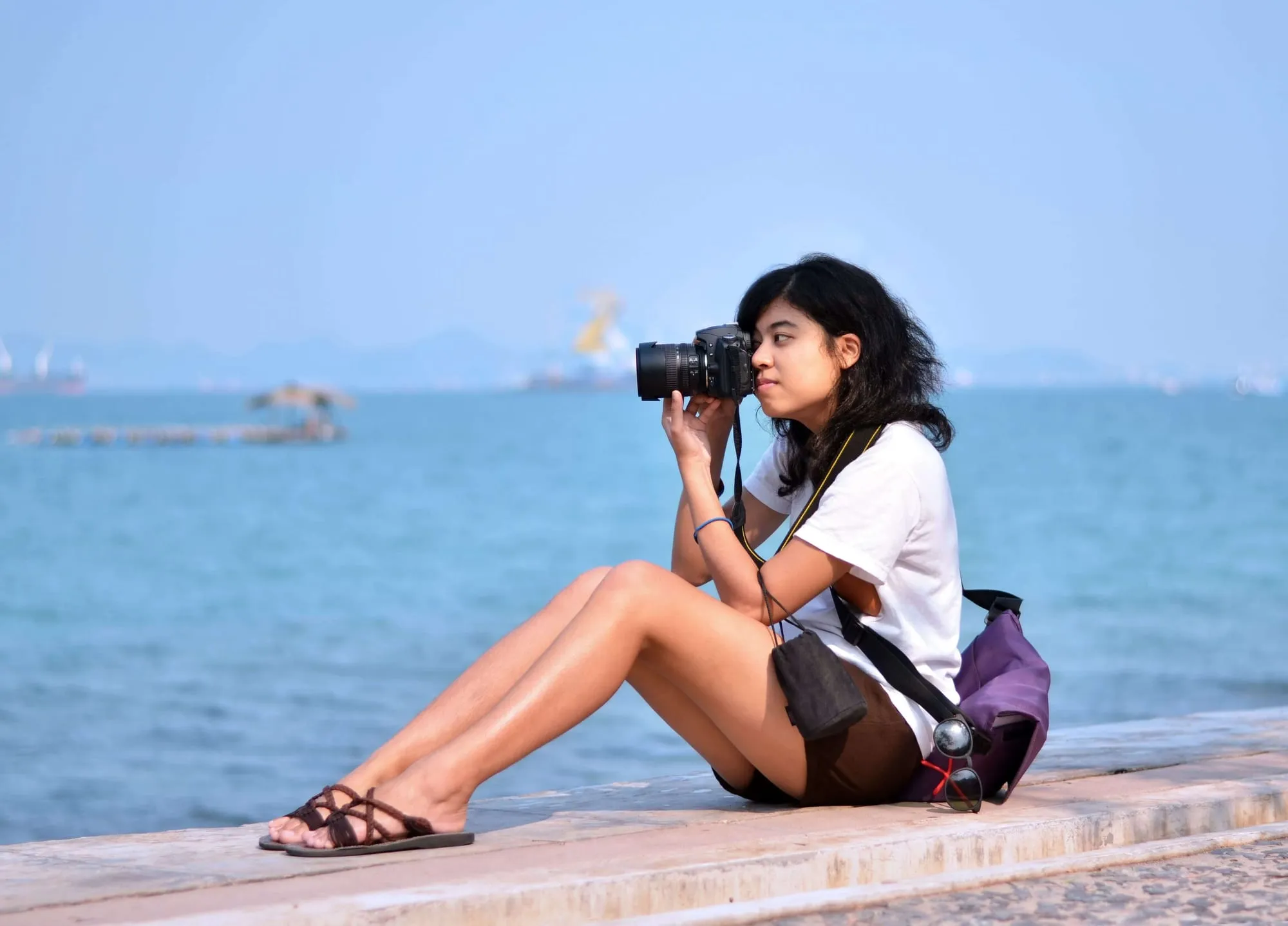 Een jonge vrouw zit aan de waterkant en fotografeert met een fototoestel