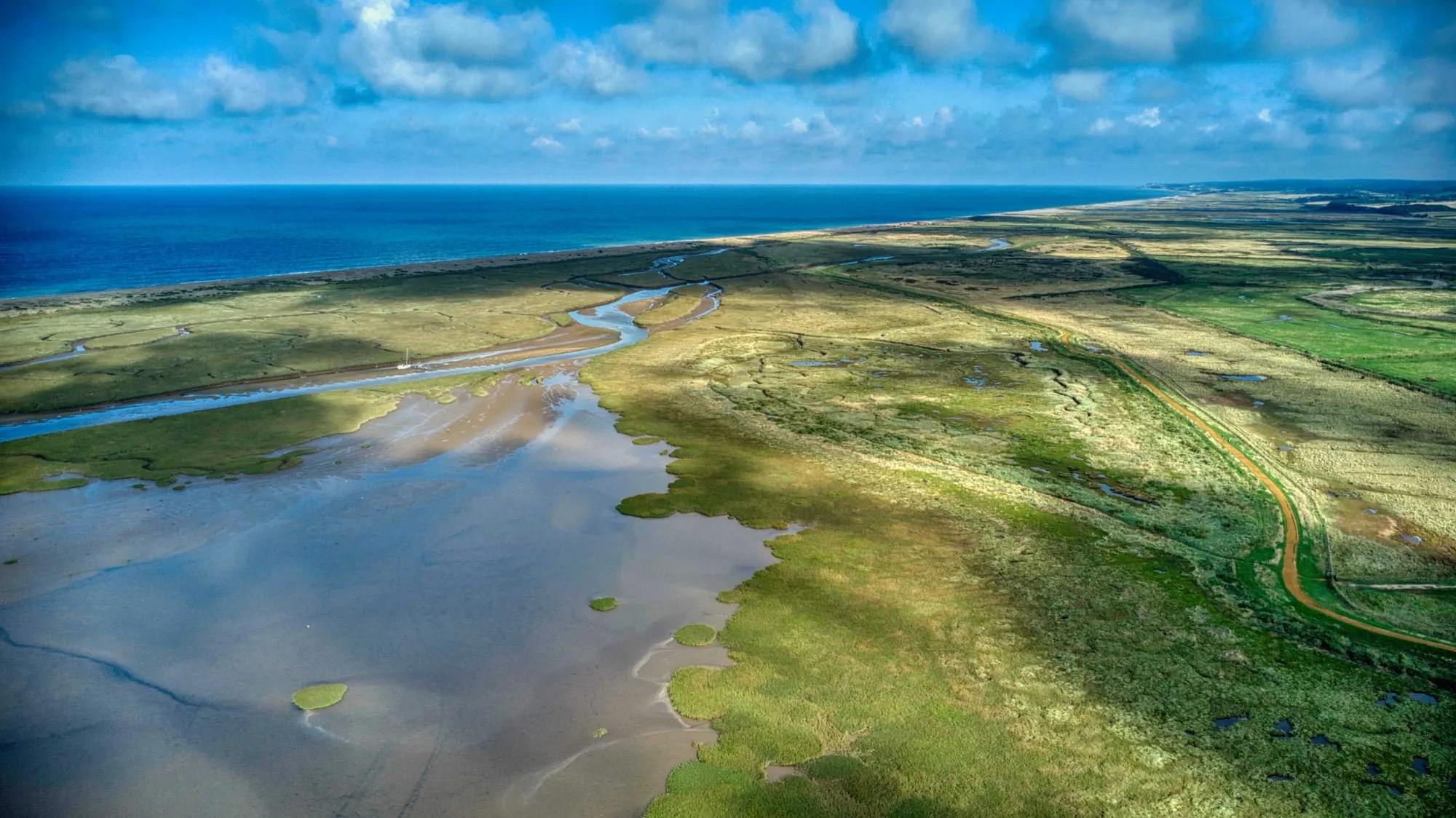 Luchtfoto van een kustlandschap met kronkelende kreken en groene schorren tot aan de zee