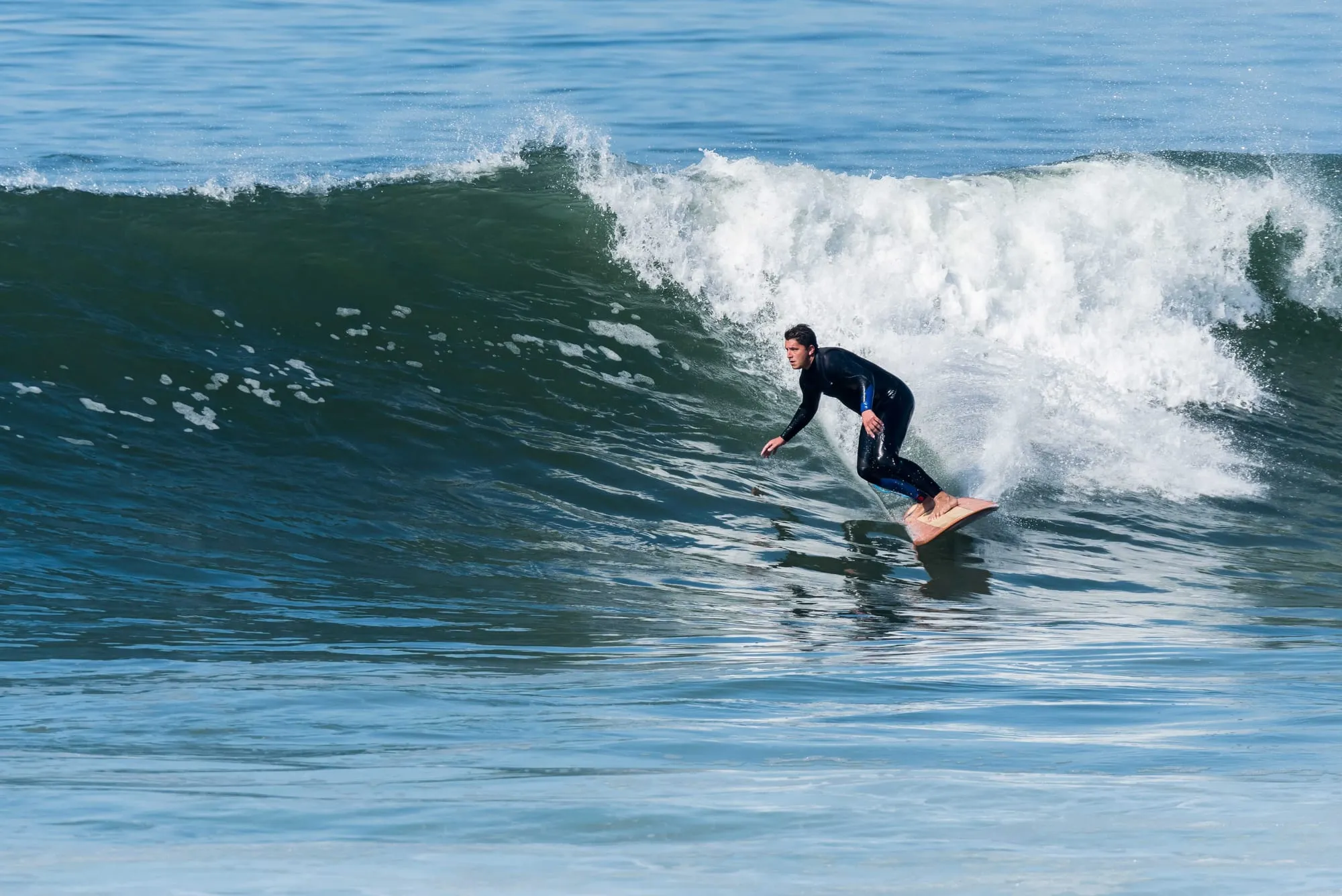 Een surfer in een zwart pak surft op een golf met wit schuim