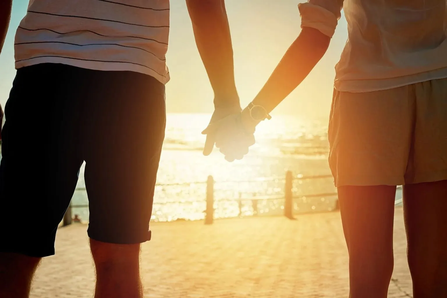 Een koppel houdt elkaars hand vast bij zonsondergang op een promenade aan zee